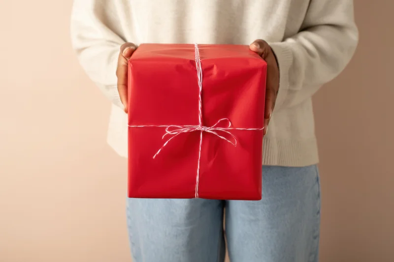 Woman holding a red wrapped gift box with white string bow in front of her body