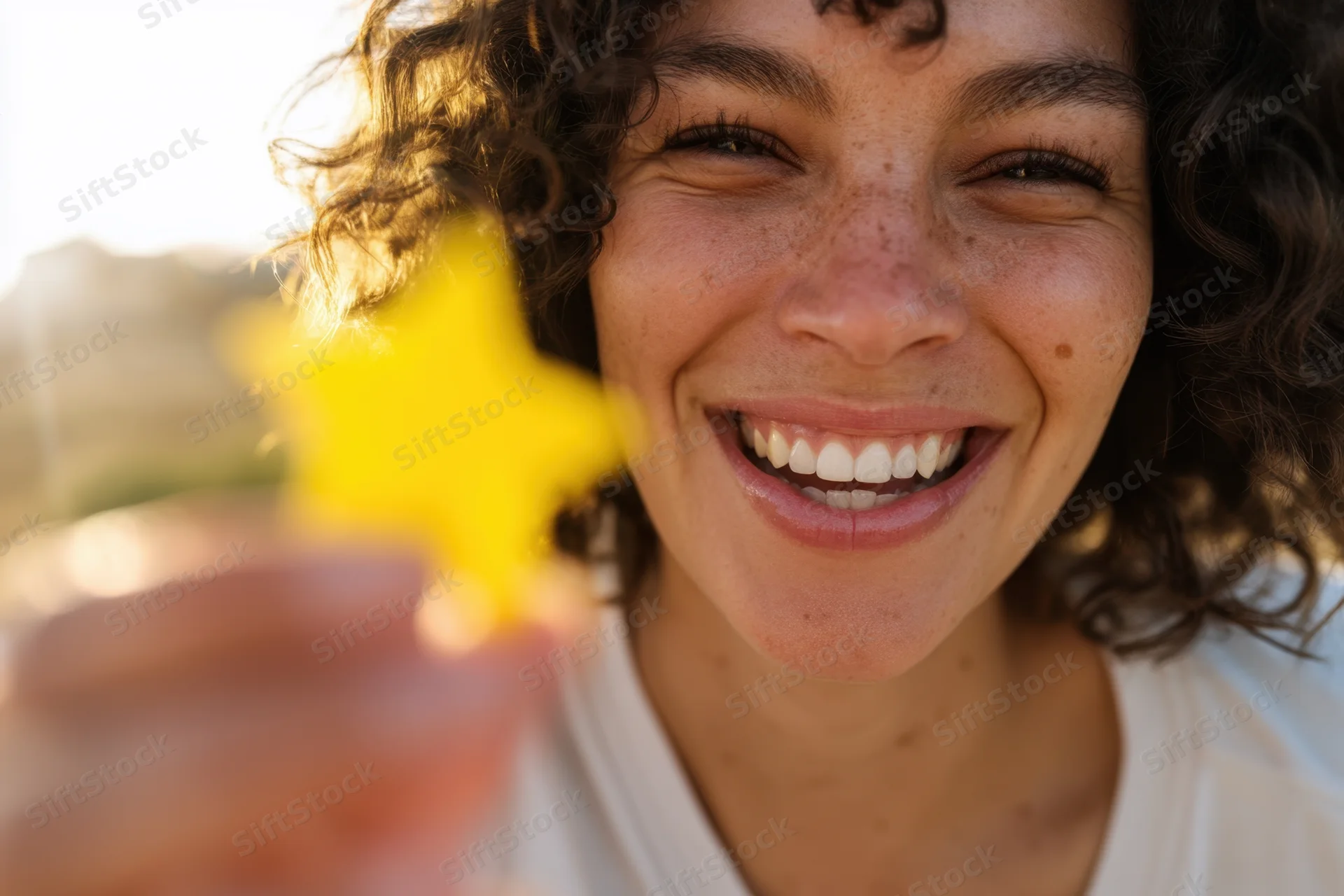 Woman smiling while holding a yellow star-shaped object outdoors in warm sunlight
