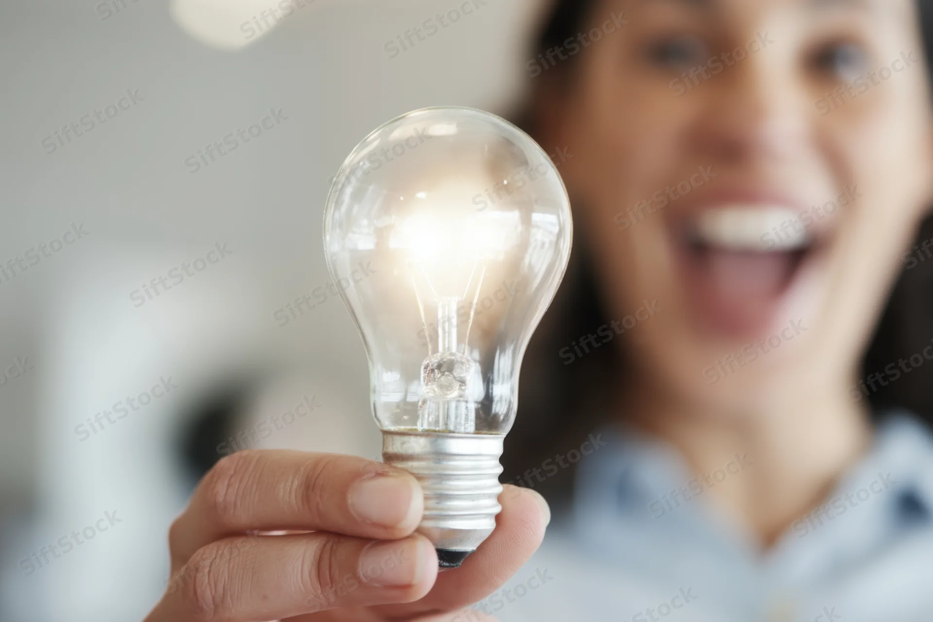 Woman holding glowing lightbulb in hand with excited expression indoors