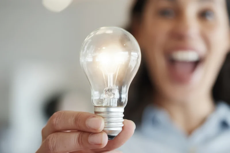 Woman holding glowing lightbulb in hand with excited expression indoors