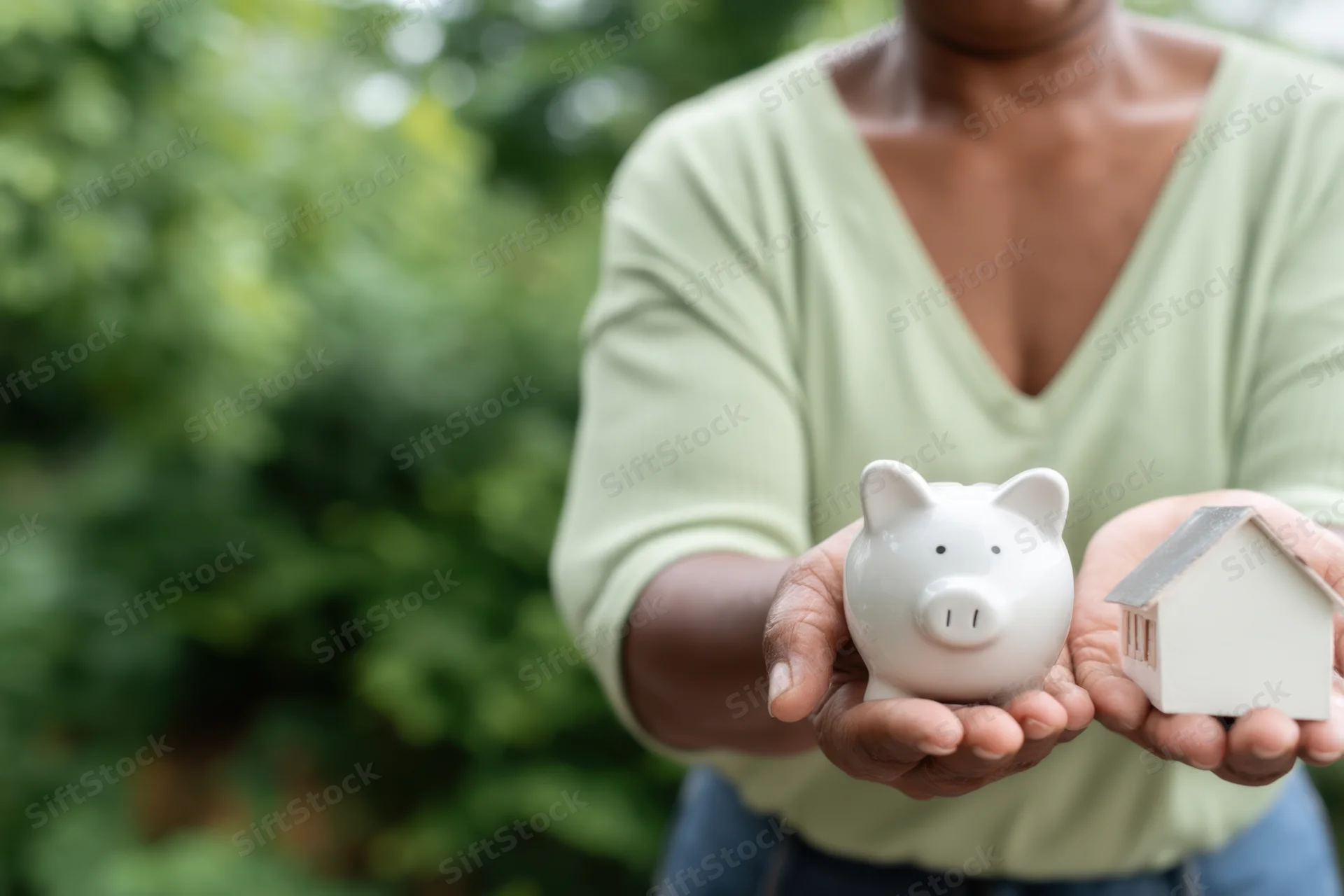 Woman holding a piggy bank and a small house model outdoors in a garden setting