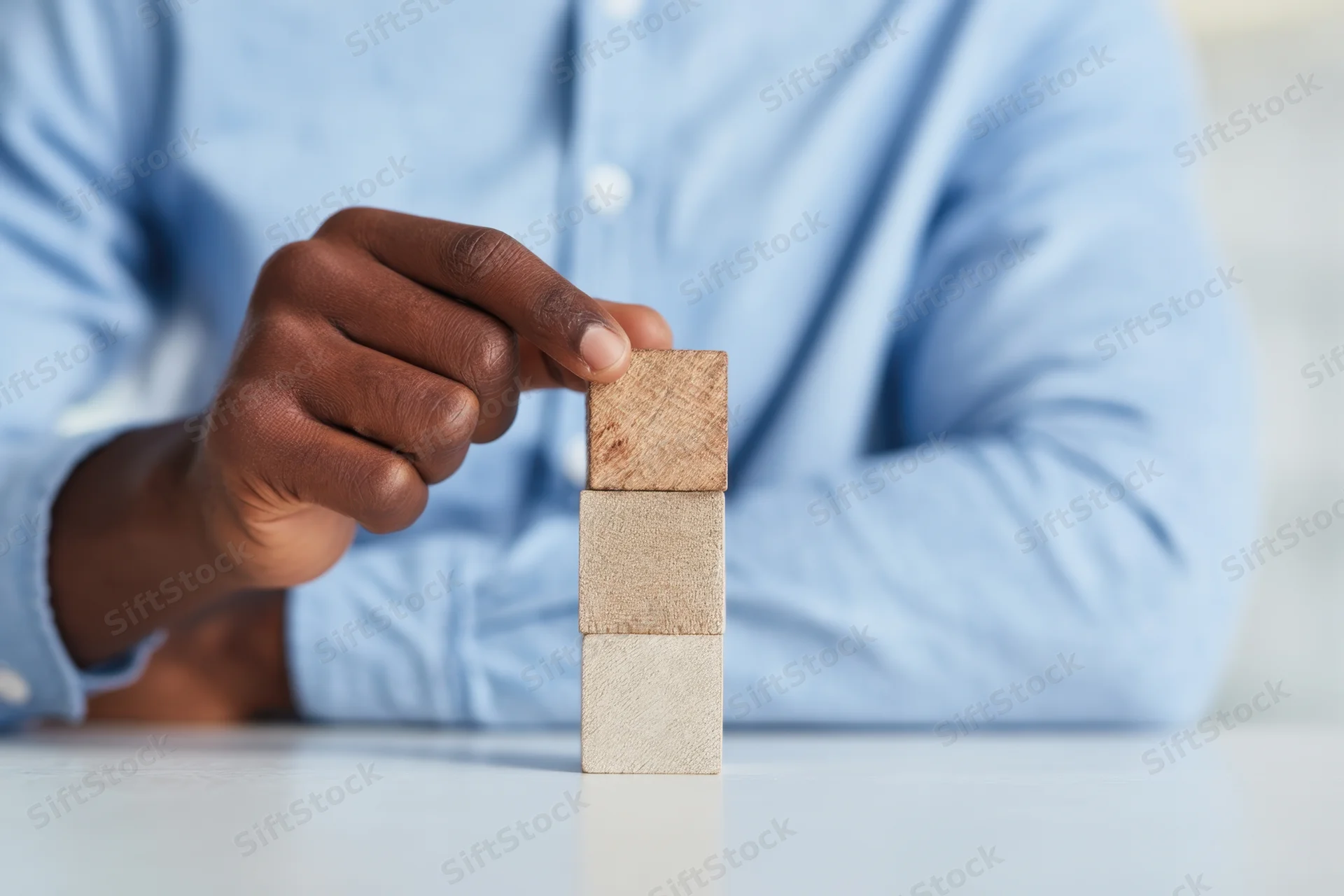 Man in light blue shirt carefully stacking wooden blocks on a white table