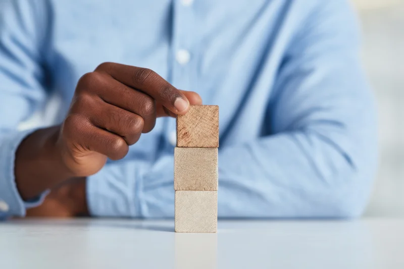 Man in light blue shirt carefully stacking wooden blocks on a white table