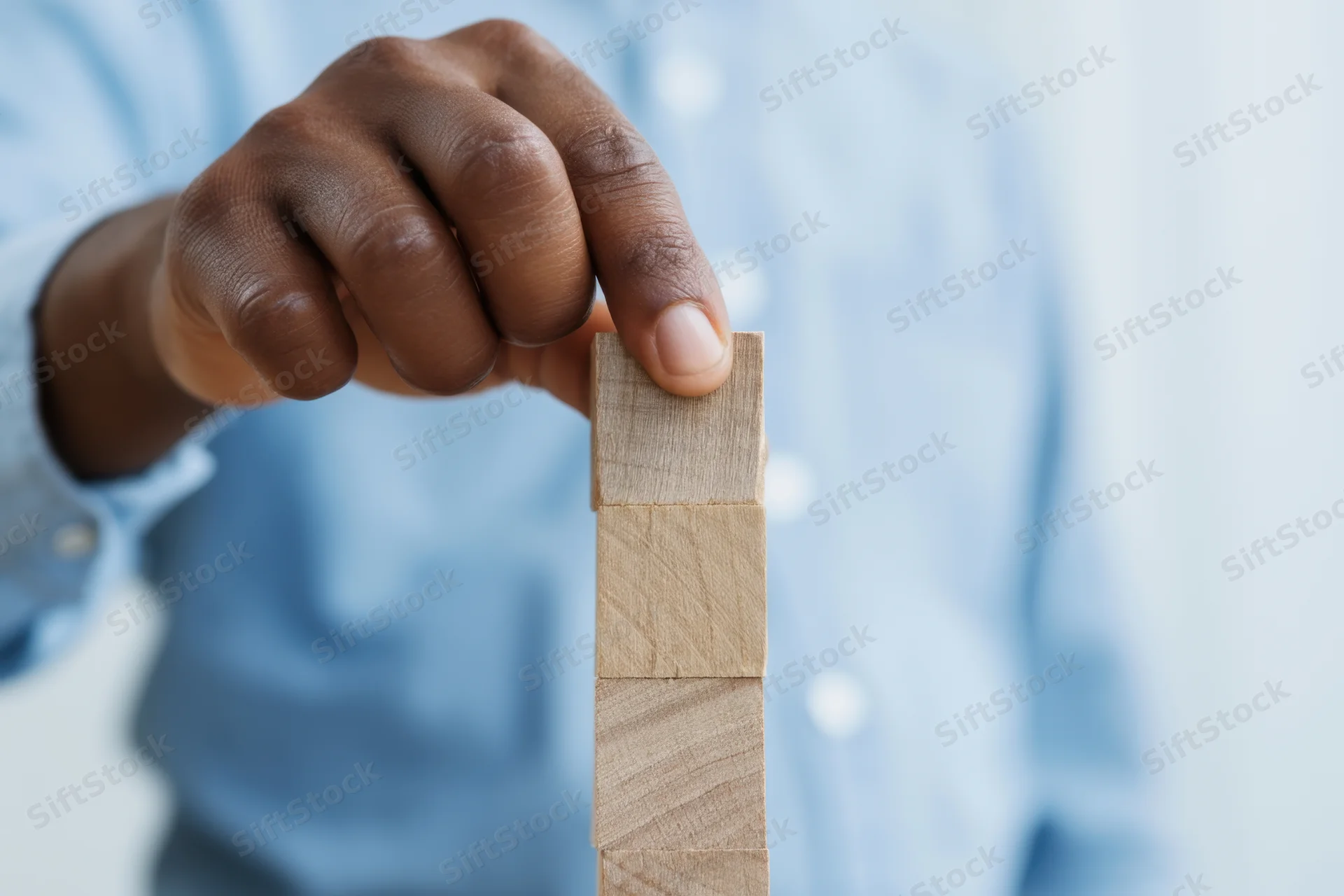 Hand placing wooden block on top of a stack of blocks in a light blue shirt