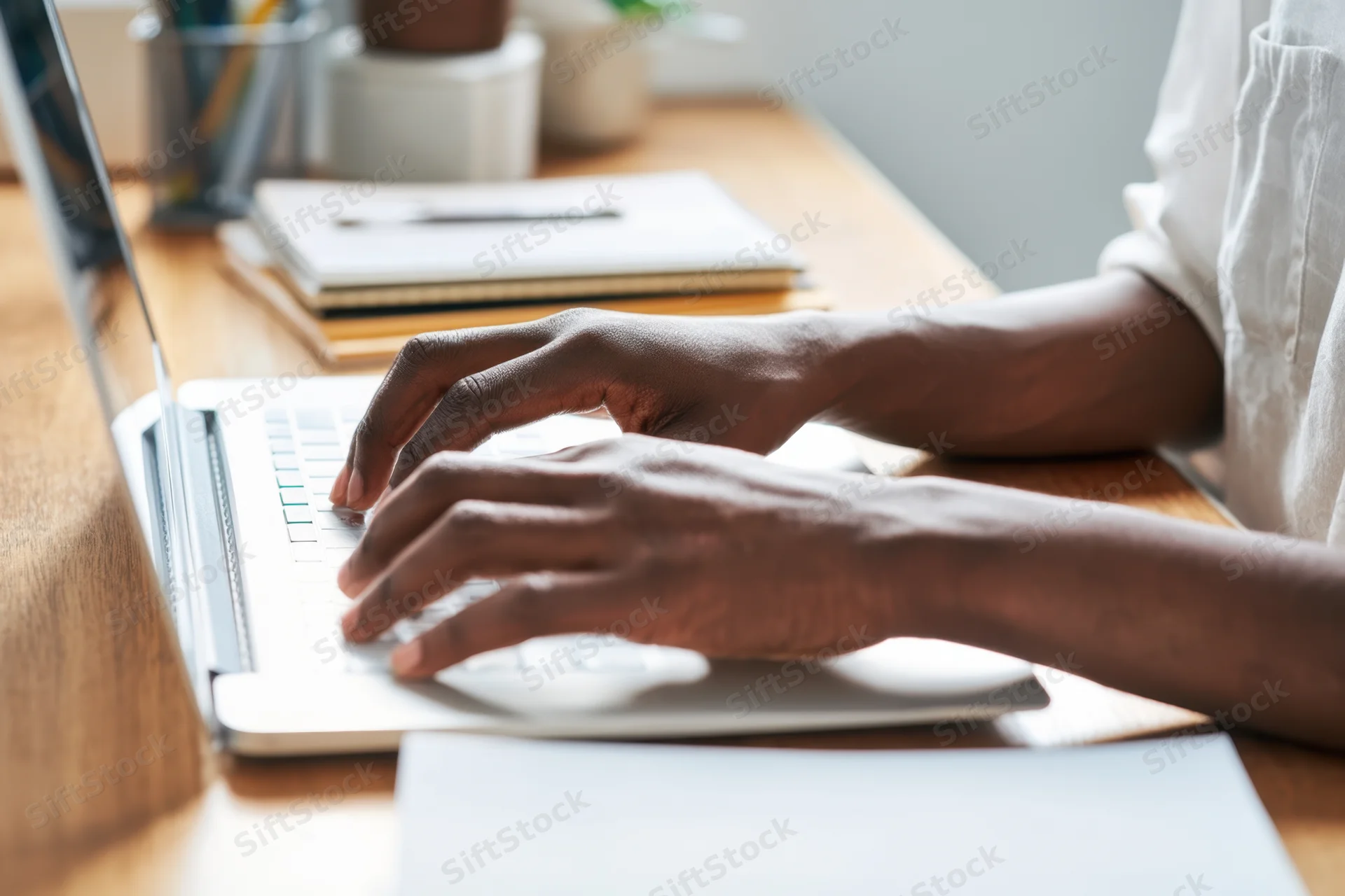 Woman typing on laptop at wooden desk in soft morning light