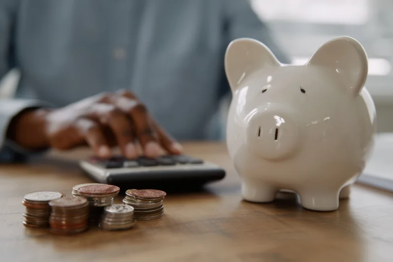 Person using calculator with coins stacked nearby on wooden desk