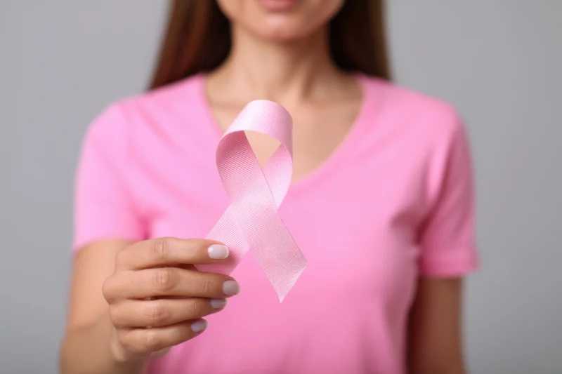 Woman holding pink ribbon symbol in hand against neutral background