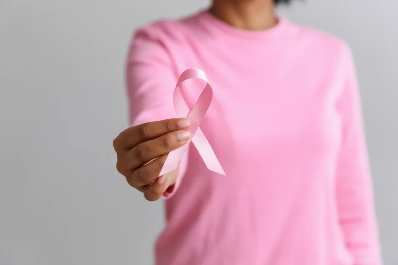 Woman holding pink ribbon symbol in hand against light gray background