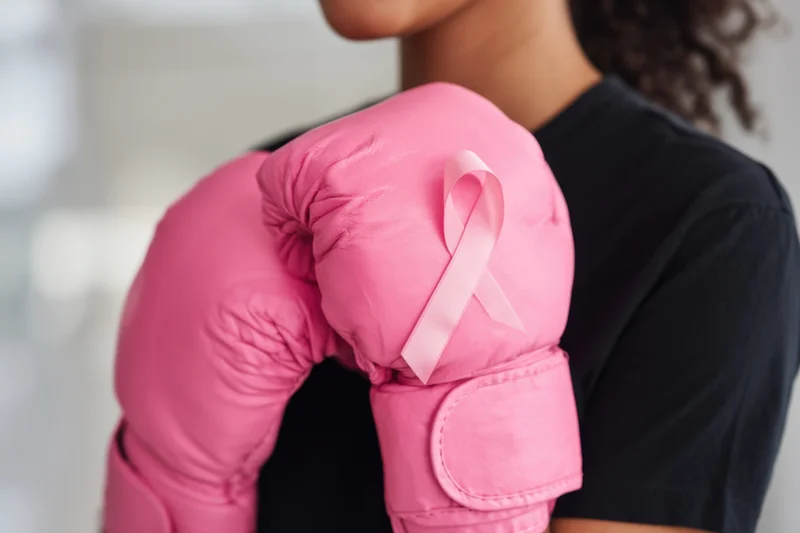 Woman wearing pink boxing gloves with breast cancer awareness ribbon, close-up on torso and arms