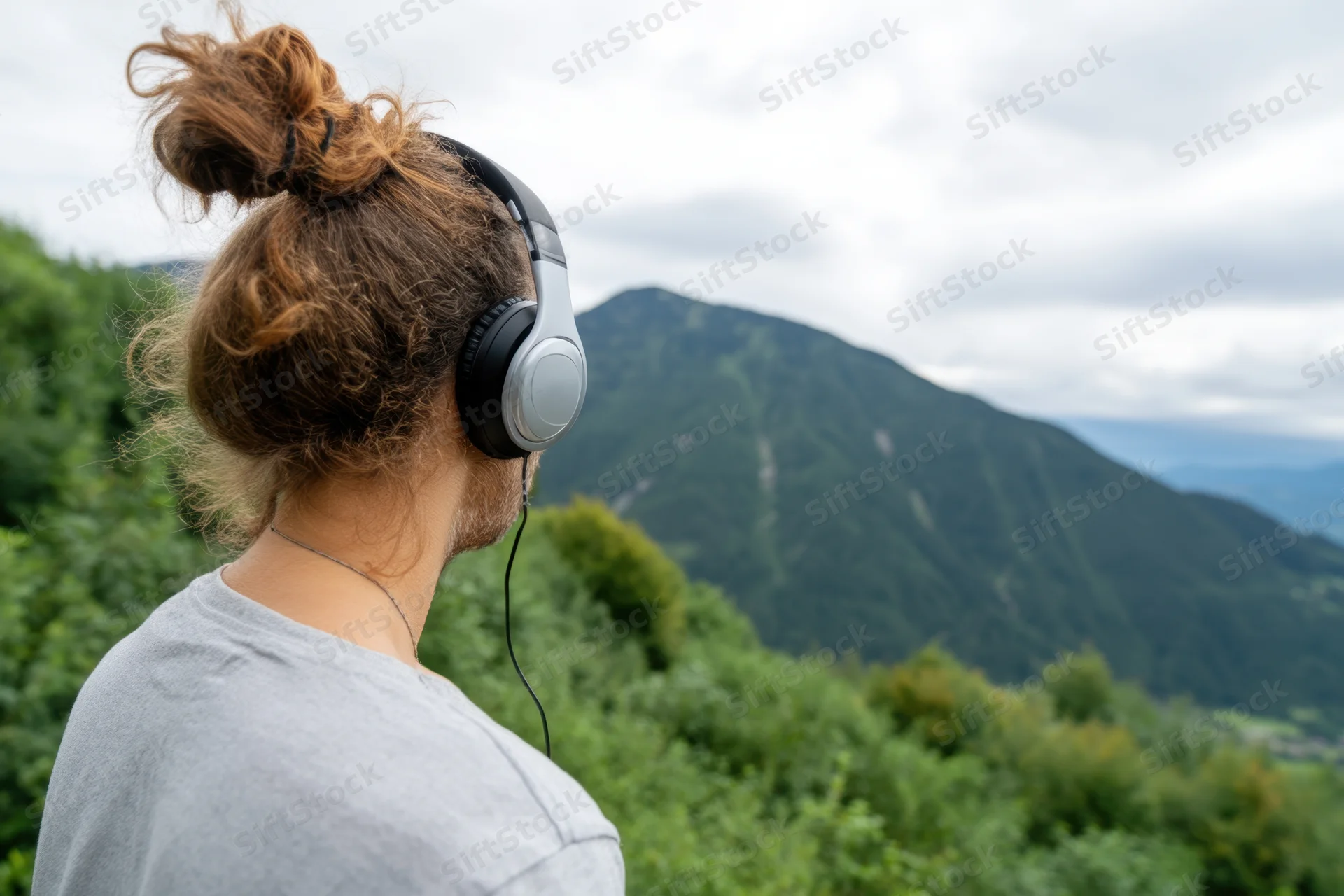 Man with headphones standing in a lush green mountain landscape