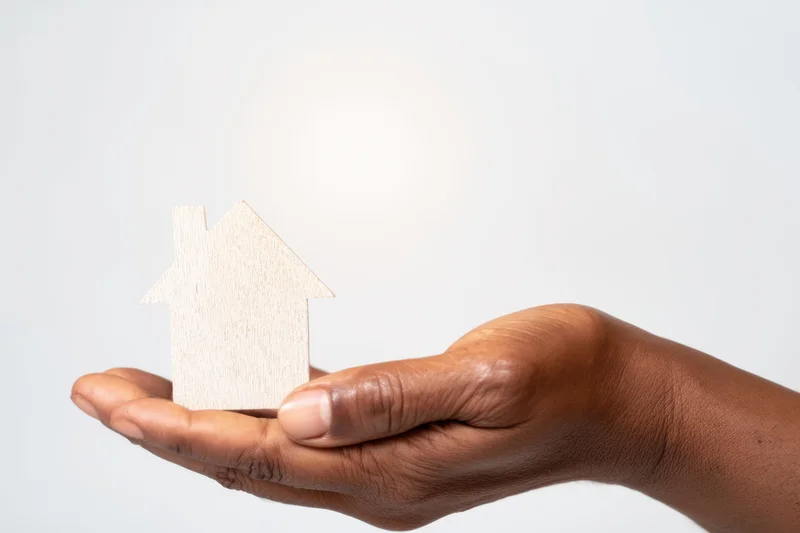 Hand holding wooden house silhouette against white background