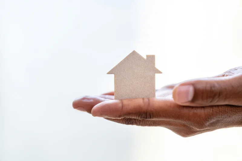 Hand holding small wooden house silhouette against bright background
