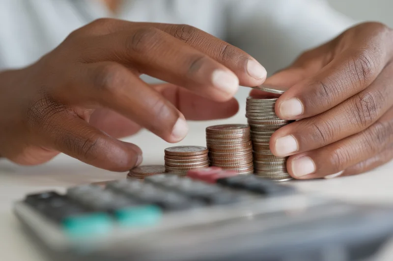 Hands stacking coins in increasing height next to a calculator on a table