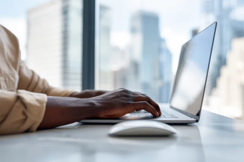 Man typing on laptop at desk with city view through window