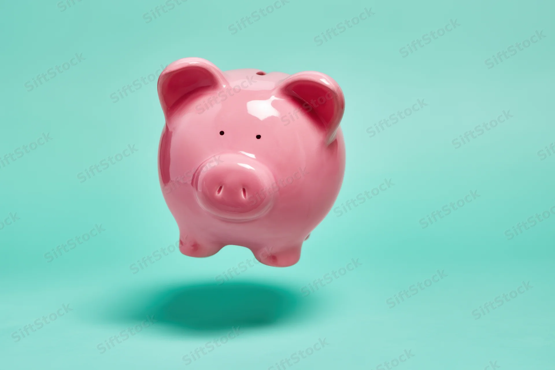 Pink ceramic piggy bank floating against a turquoise gradient background