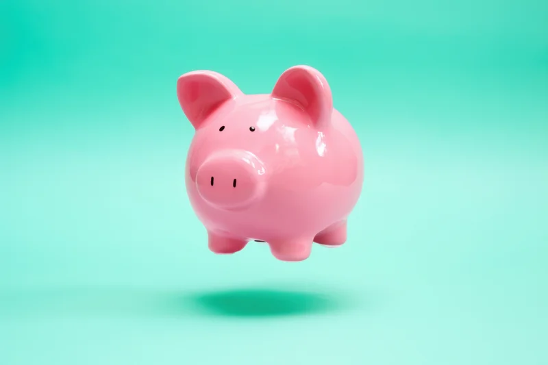 Pink ceramic piggy bank floating against a soft green gradient background