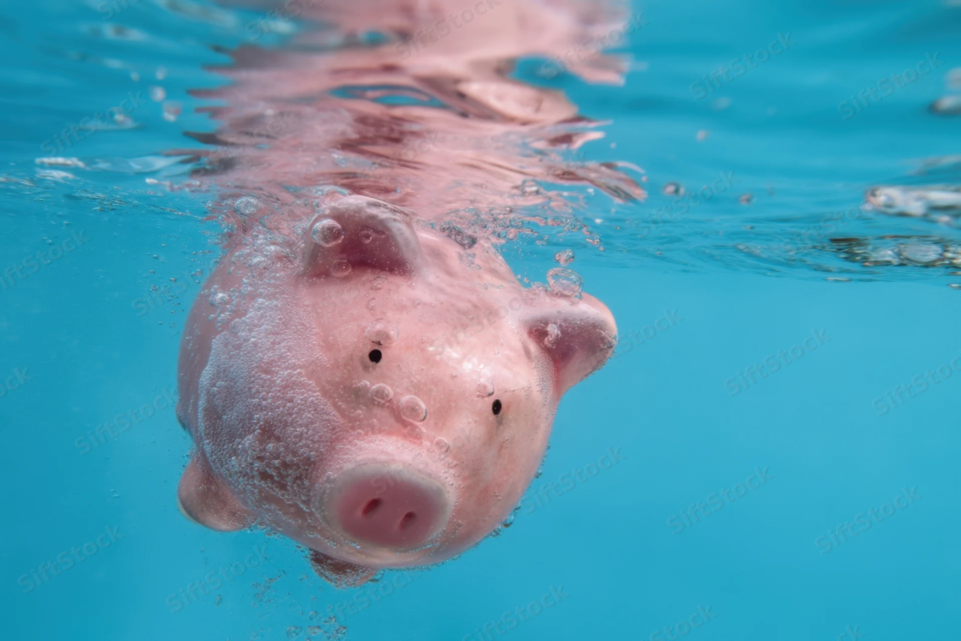 Pink piggy bank floating partially submerged in clear blue water