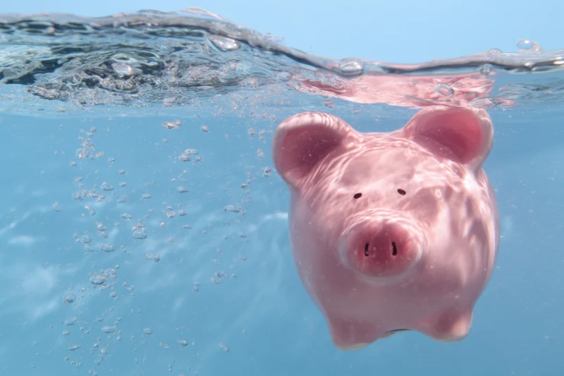 Pink piggy bank floating underwater in clear blue water with bubbles rising around it