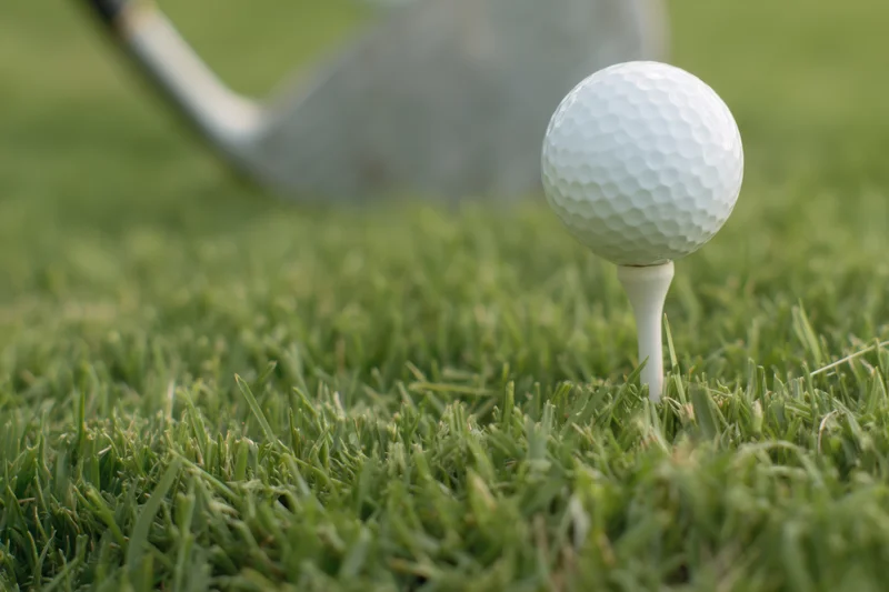 Golf ball on tee in green grass with golf club in background