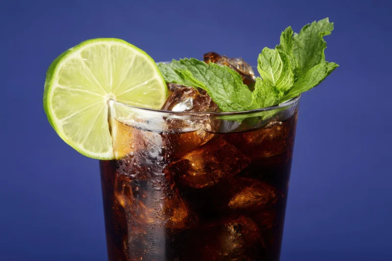 Glass of cola with ice and lime garnish against blue background