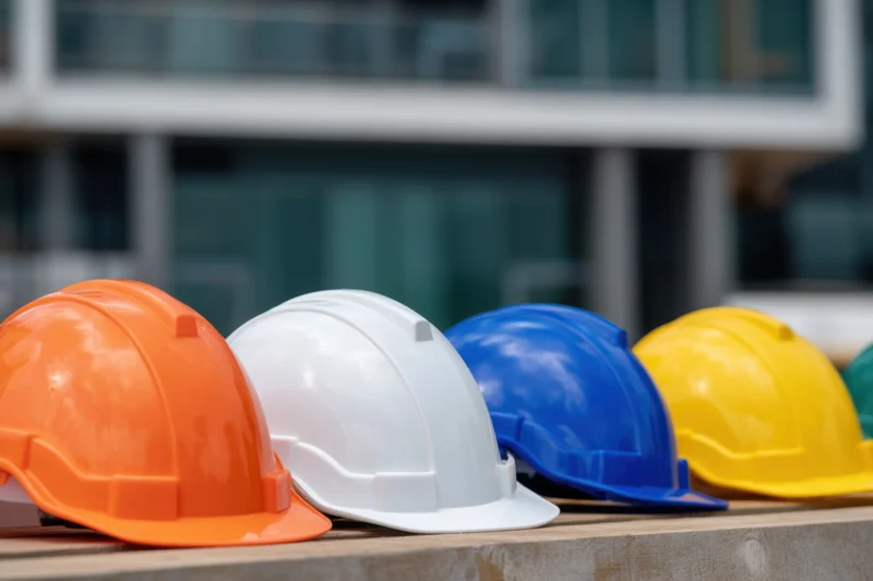 Row of colorful construction hardhats arranged on a ledge in front of a modern building facade