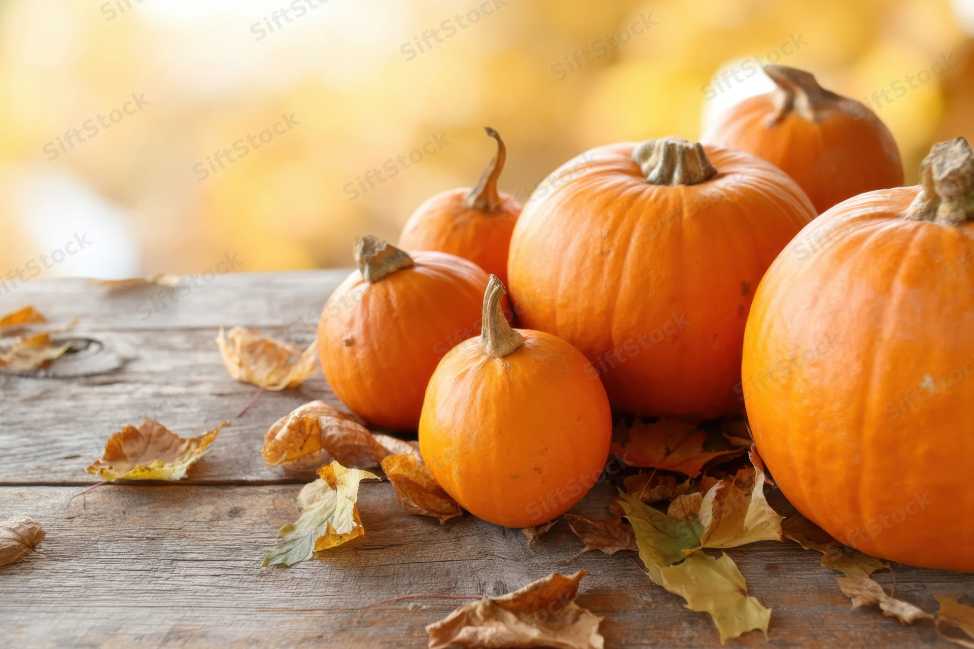 Pumpkins arranged on a rustic wooden table with scattered autumn leaves