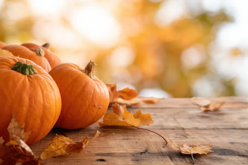 Pumpkins and dry maple leaves arranged on a rustic wooden table with autumn bokeh background
