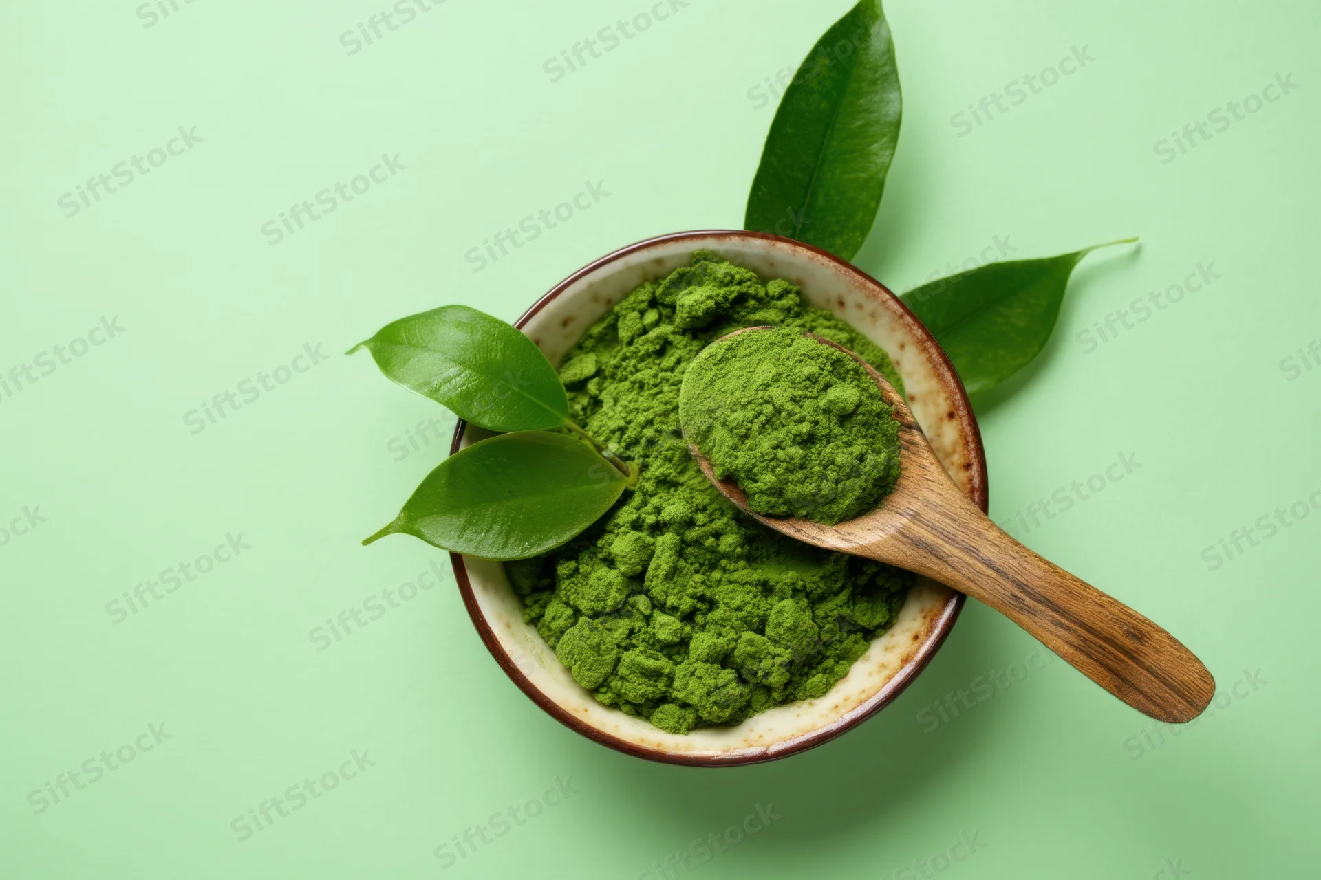 Matcha powder in a bowl with wooden spoon and green leaves on a light green background