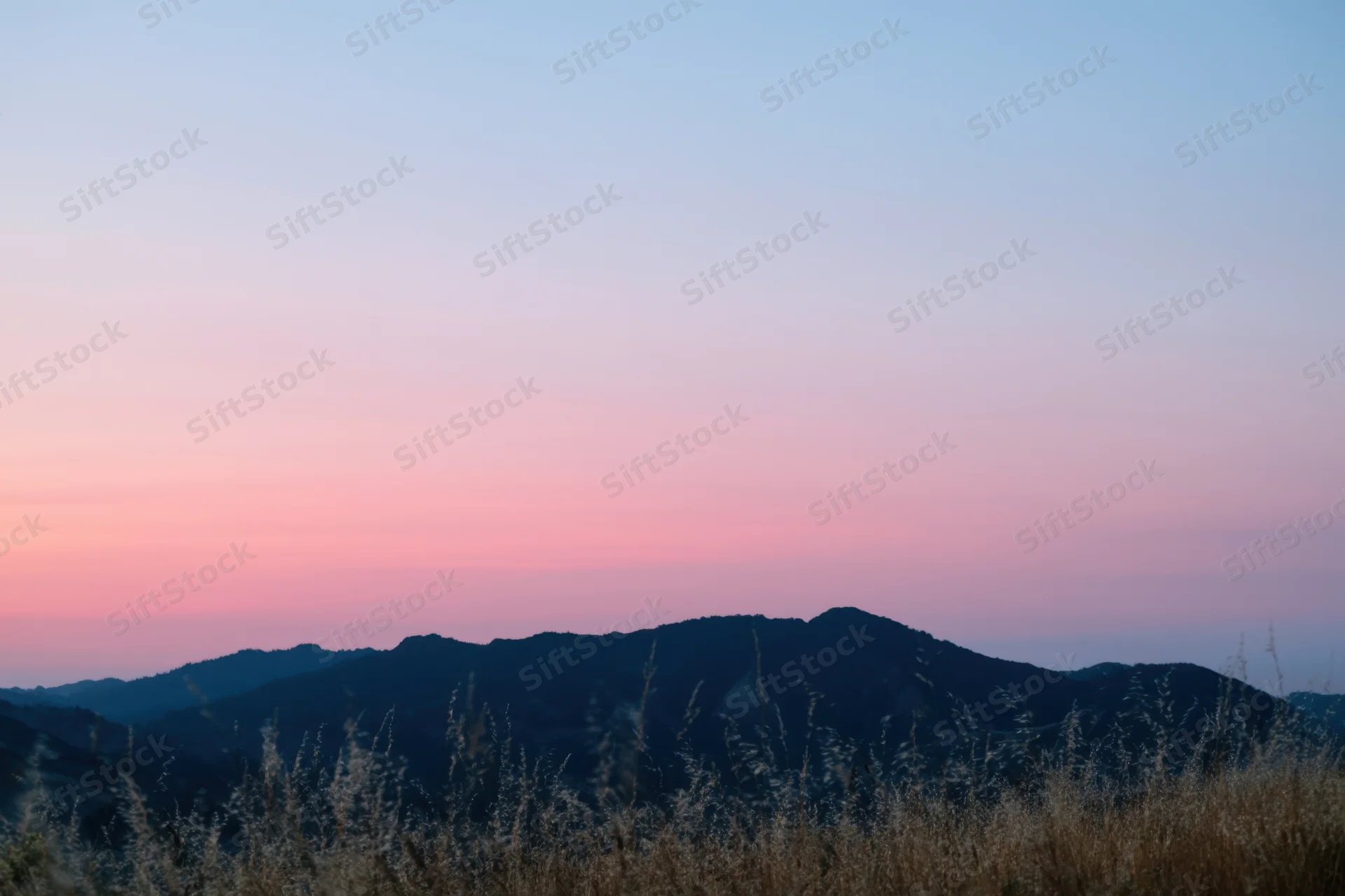 Soft hills silhouetted against a gradient dawn sky with dry grass in the foreground