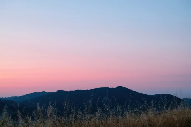 Soft hills silhouetted against a gradient dawn sky with dry grass in the foreground
