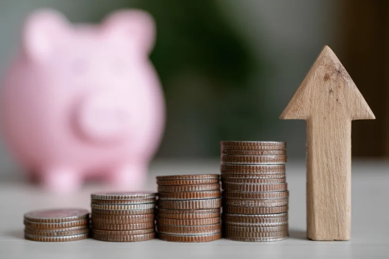 Stacked coins in ascending order with wooden arrow and pink piggy bank on tabletop