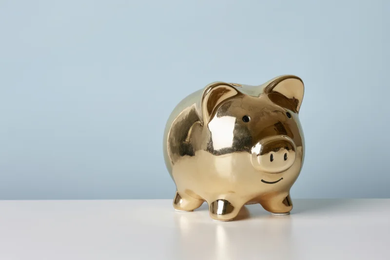 Shiny gold piggy bank standing on a white surface against a blue background
