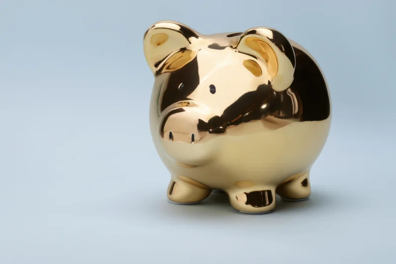 Shiny gold piggy bank standing on smooth surface against light blue background with copyspace