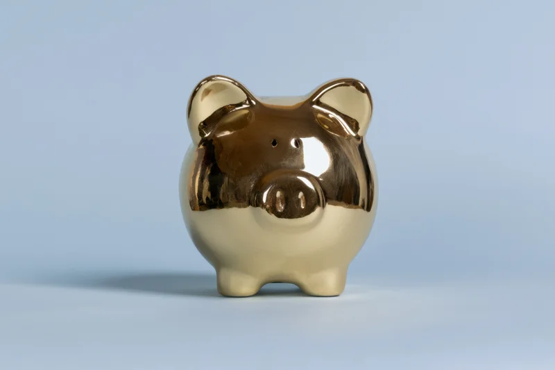 Shiny gold piggy bank standing on a smooth surface against a light blue background