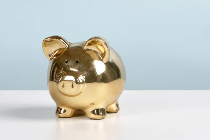 Shiny gold piggy bank sitting on white surface against light blue background