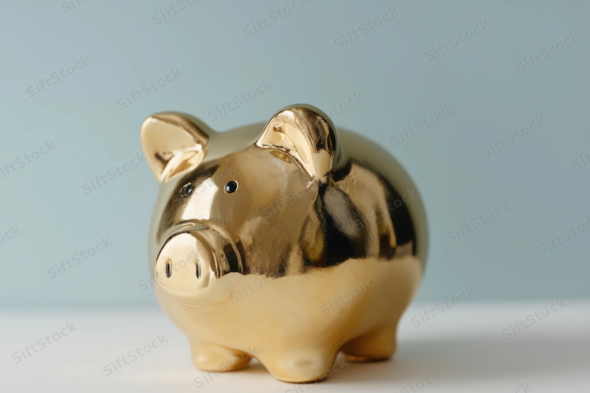 Shiny gold piggy bank sitting on white surface against light blue background