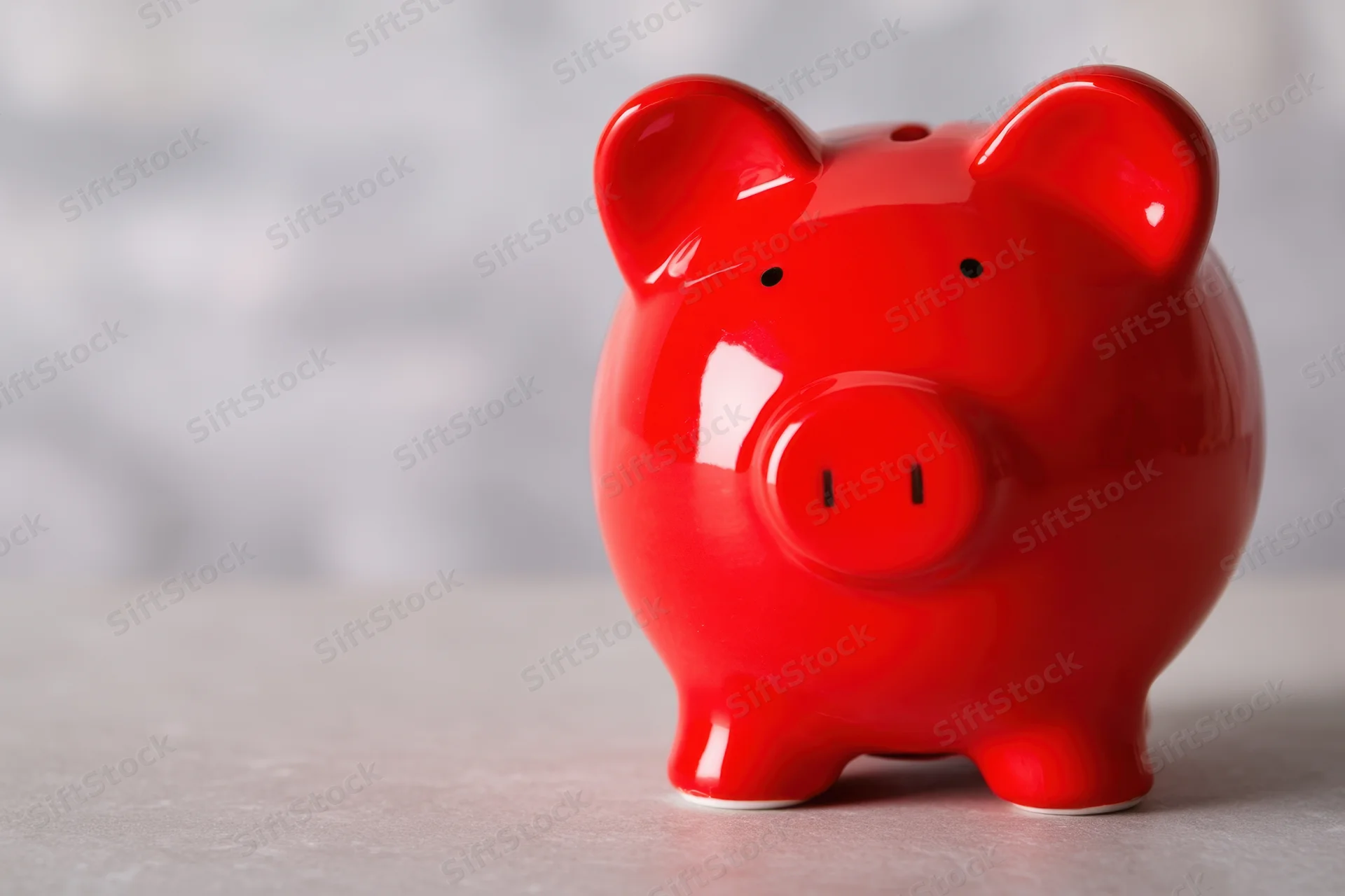 Shiny red ceramic piggy bank sitting on a light surface against a blurred background