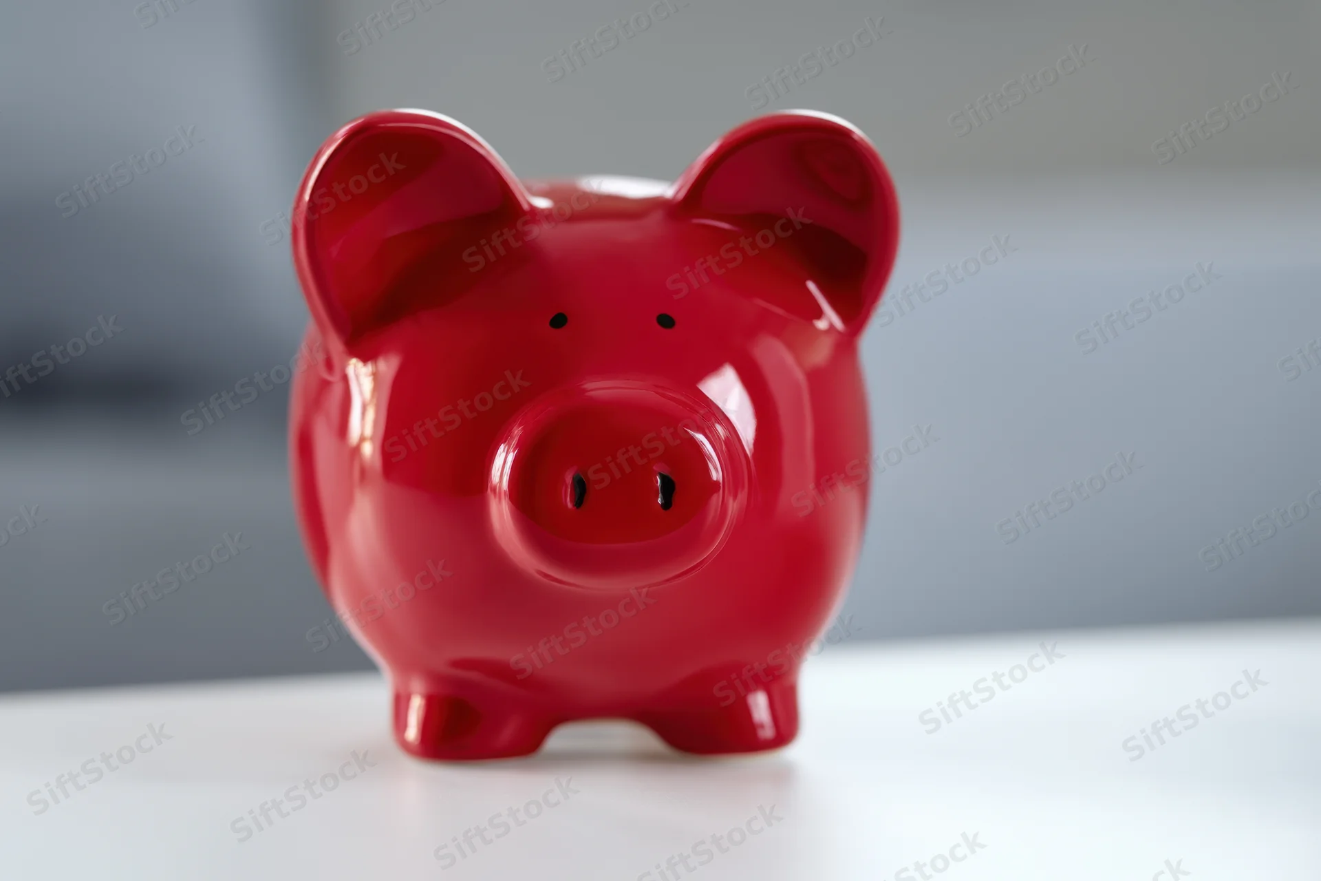 Shiny red ceramic piggy bank sitting on a white surface against a blurred background
