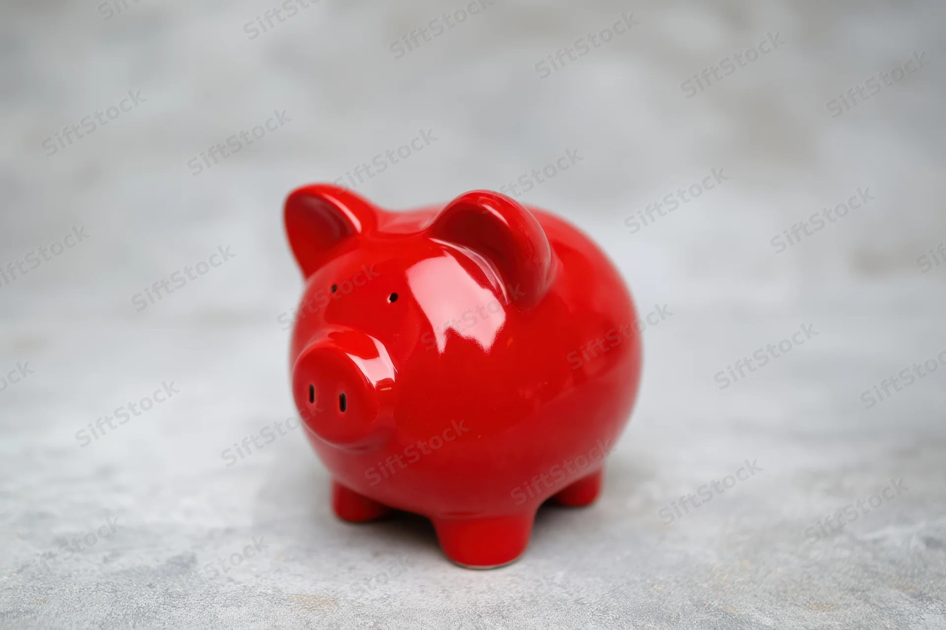 Shiny red ceramic piggy bank sitting on a textured gray surface with blurred background