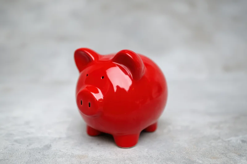 Shiny red ceramic piggy bank sitting on a textured gray surface with blurred background