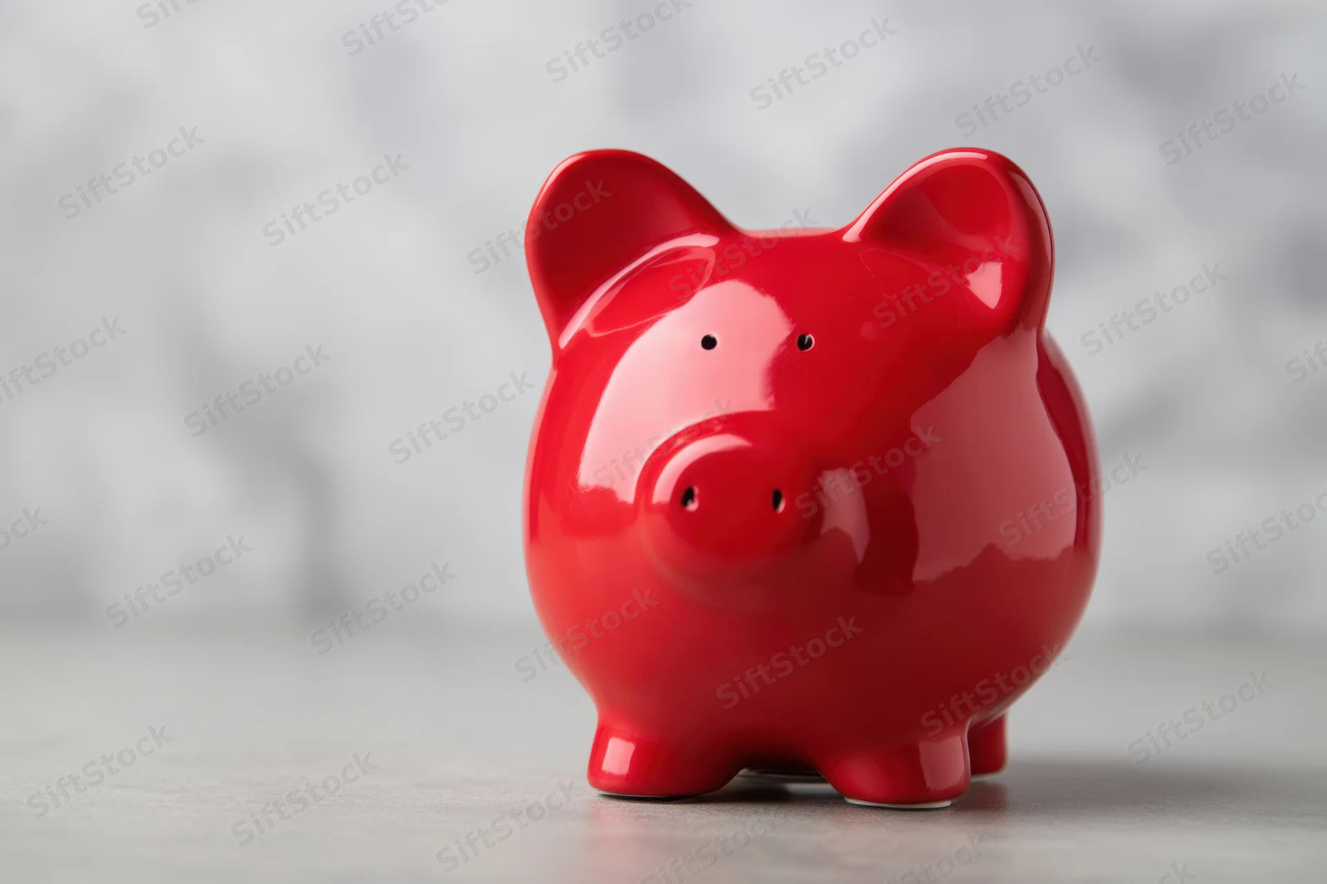 Shiny red ceramic piggy bank sitting on a light surface against a blurred background