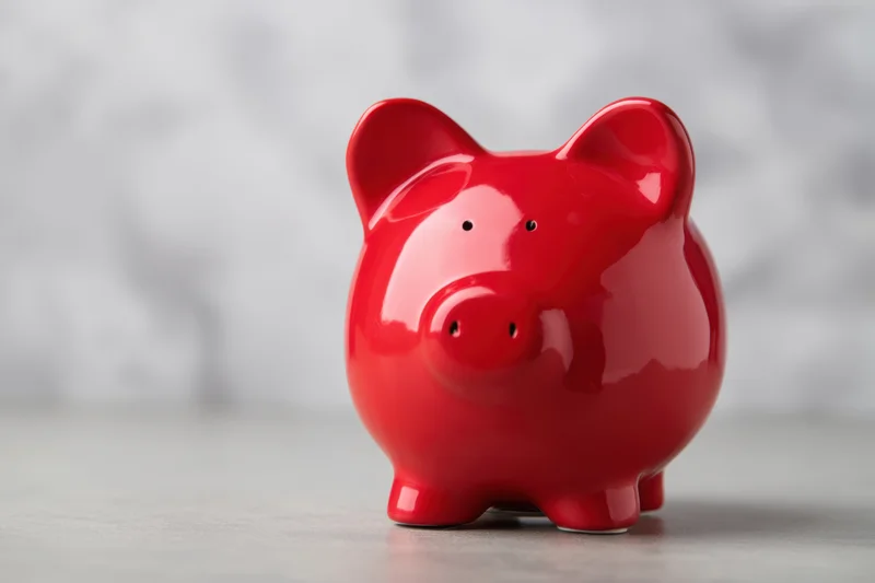 Shiny red ceramic piggy bank sitting on a light surface against a blurred background