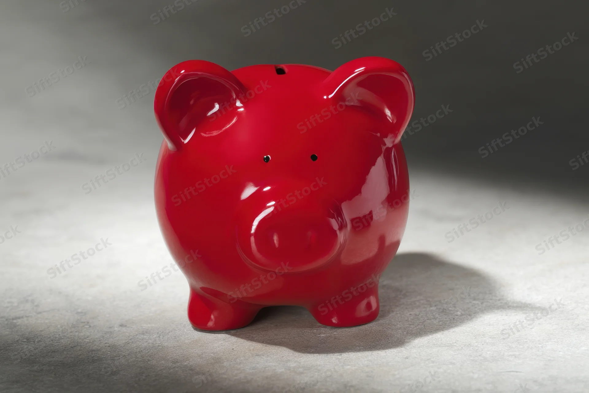 Shiny red ceramic piggy bank sitting on textured gray surface with soft shadow