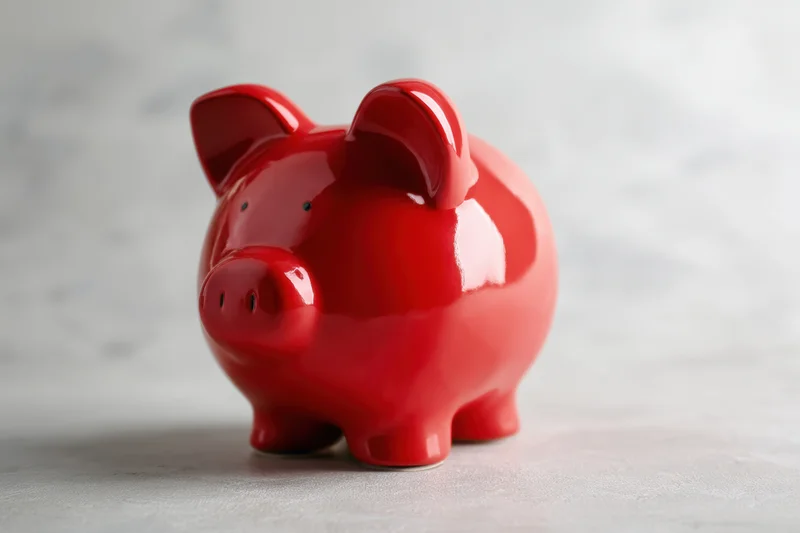 Shiny red ceramic piggy bank sitting on textured gray surface with copyspace