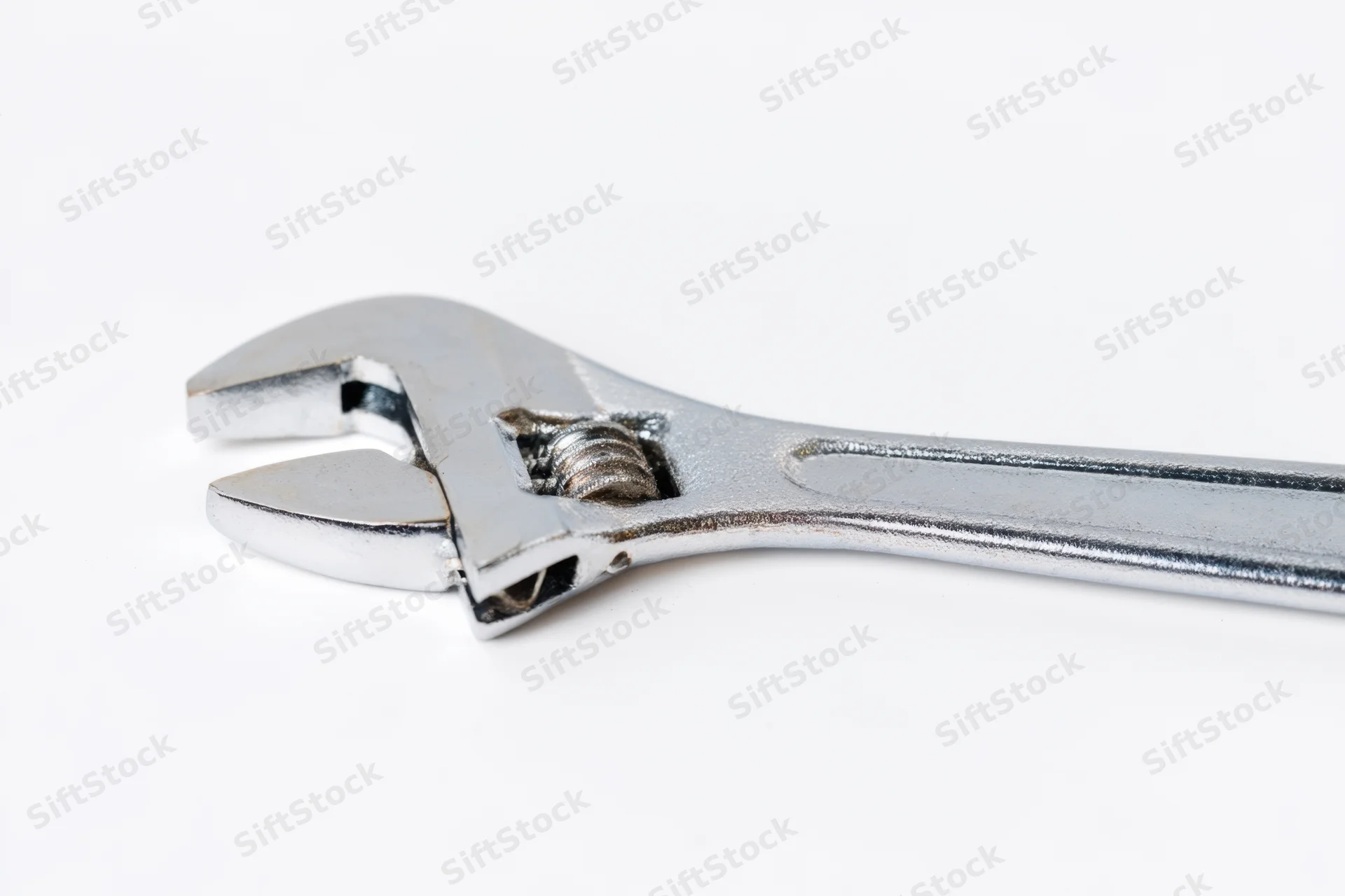 Shiny silver adjustable wrench laid flat on a white surface
