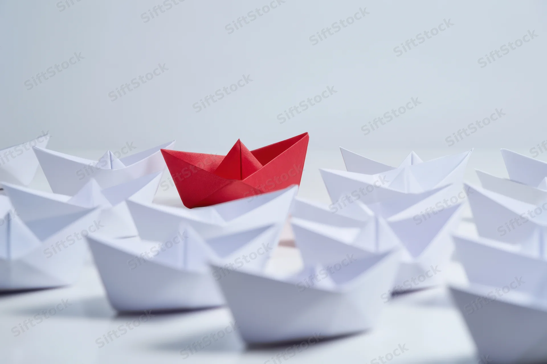 Single red paper boat centered among white boats on a plain surface