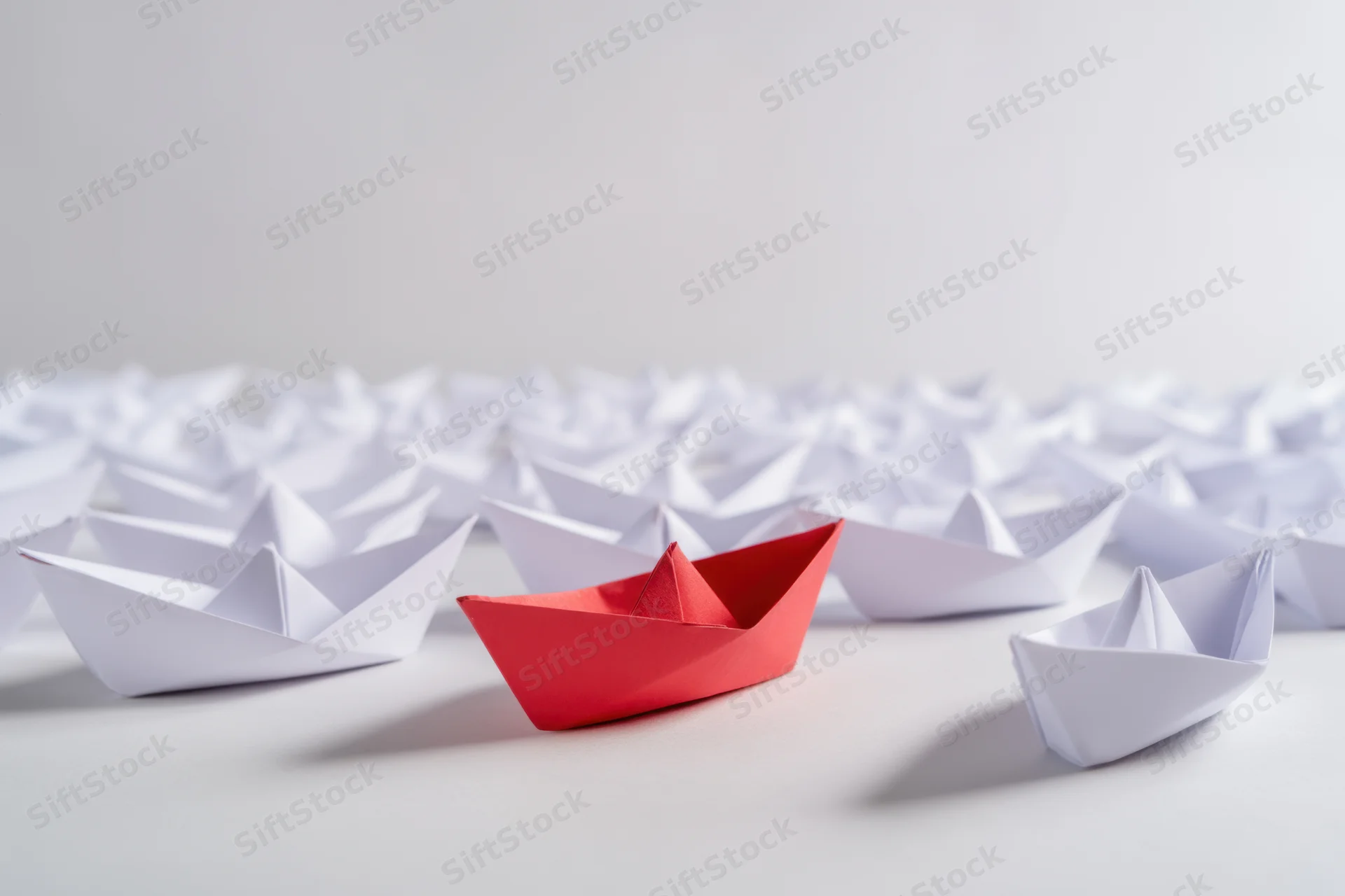 Red paper boat among white boats on a plain surface