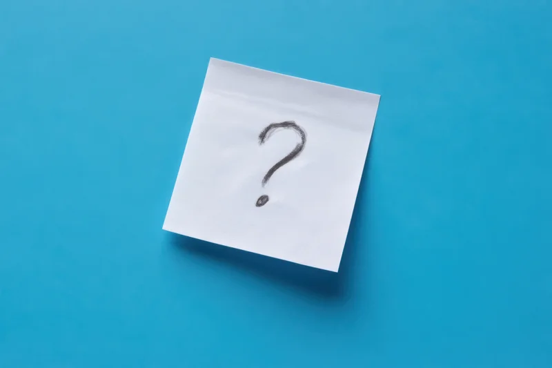 White sticky note with hand-drawn question mark on blue background
