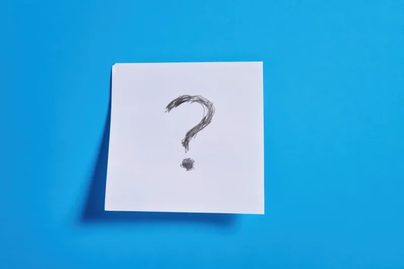 Handdrawn question mark on a white paper note against a blue background