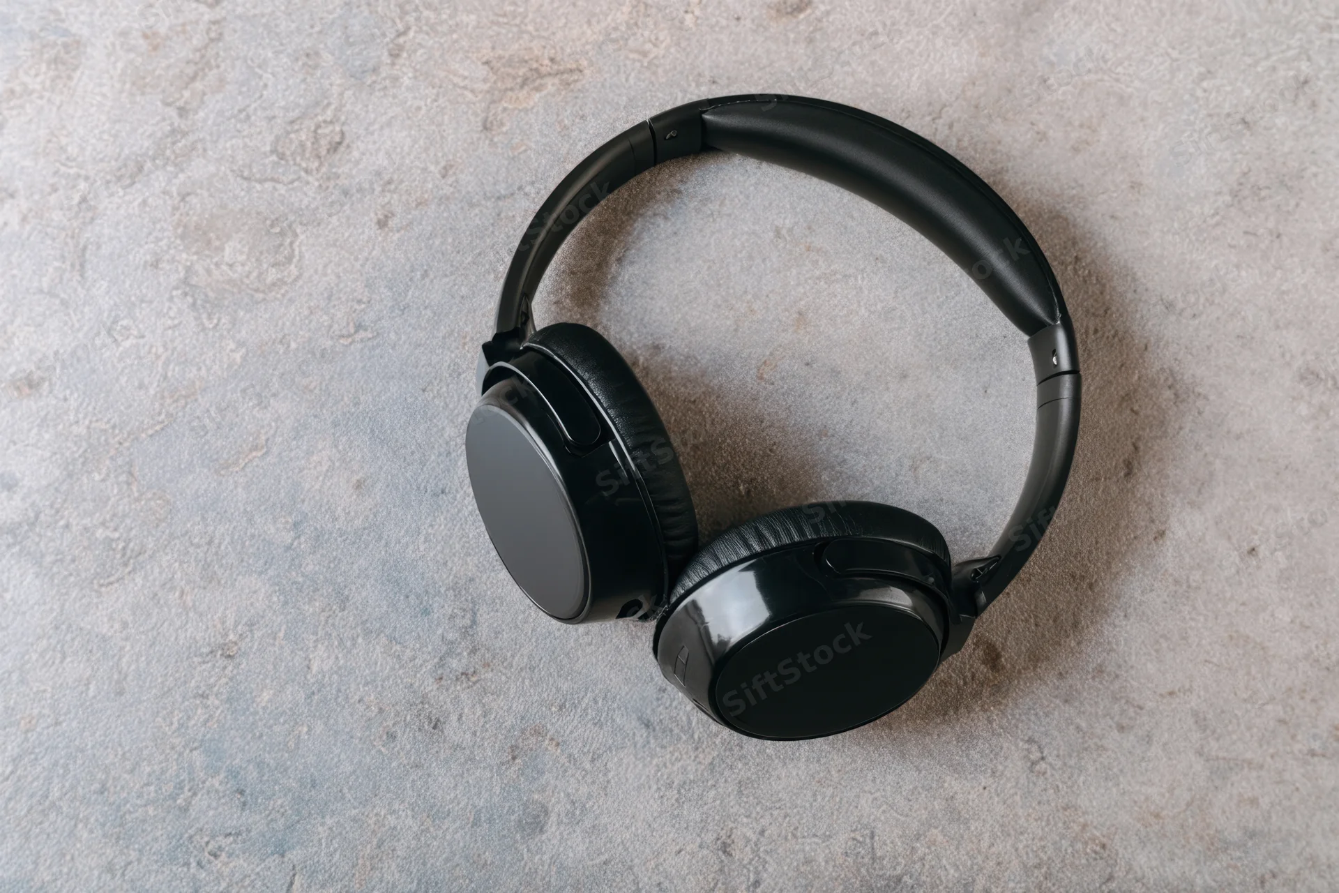 Black wireless over-ear headphones resting on textured gray stone surface in flat lay view
